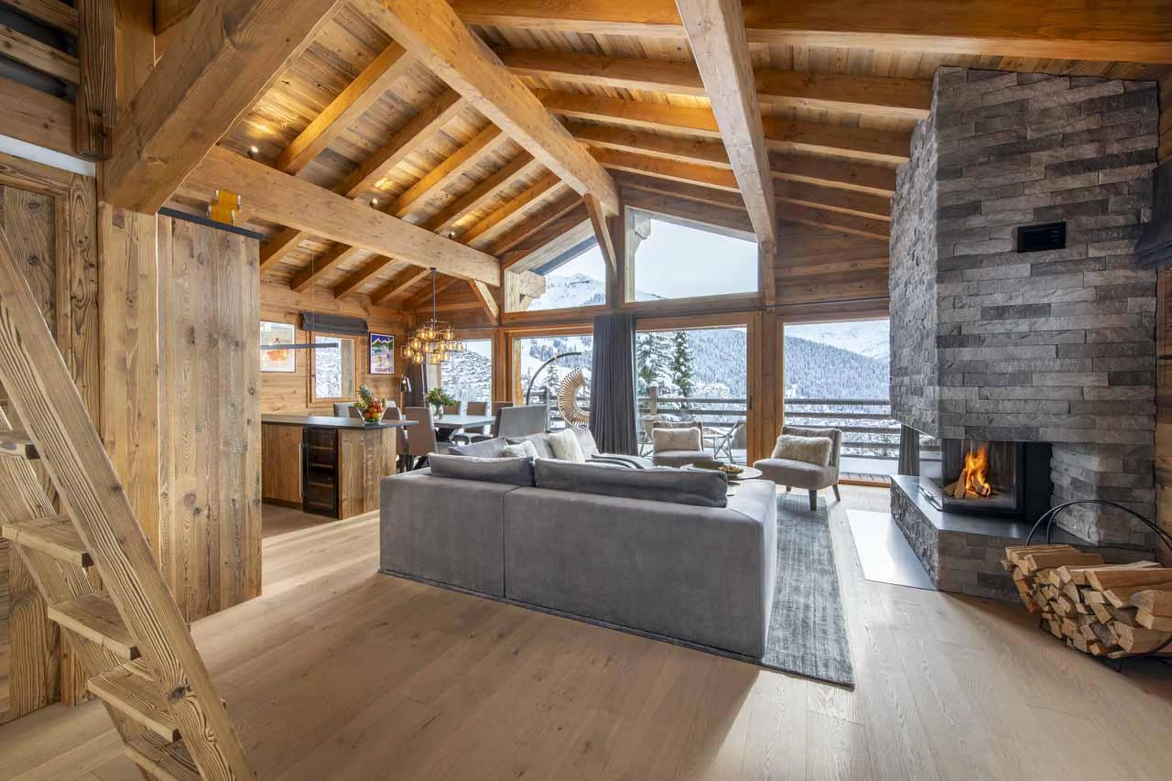 L-shaped sofa and armchairs surrounding the stone fireplace at Chalet Cortil in Verbier