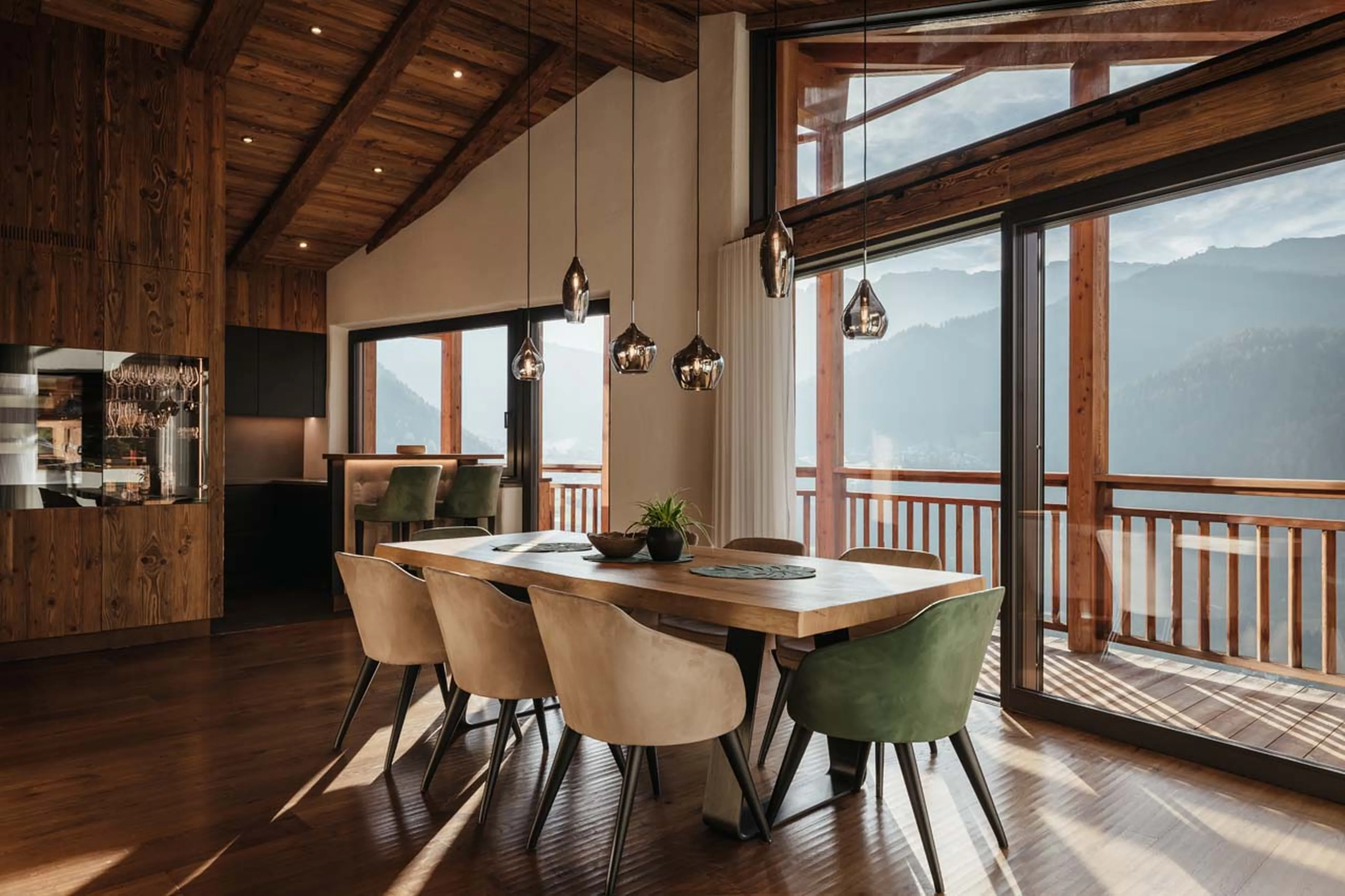 Dining table beneath expansive glass windows in Chalet Filip, Val Gardena