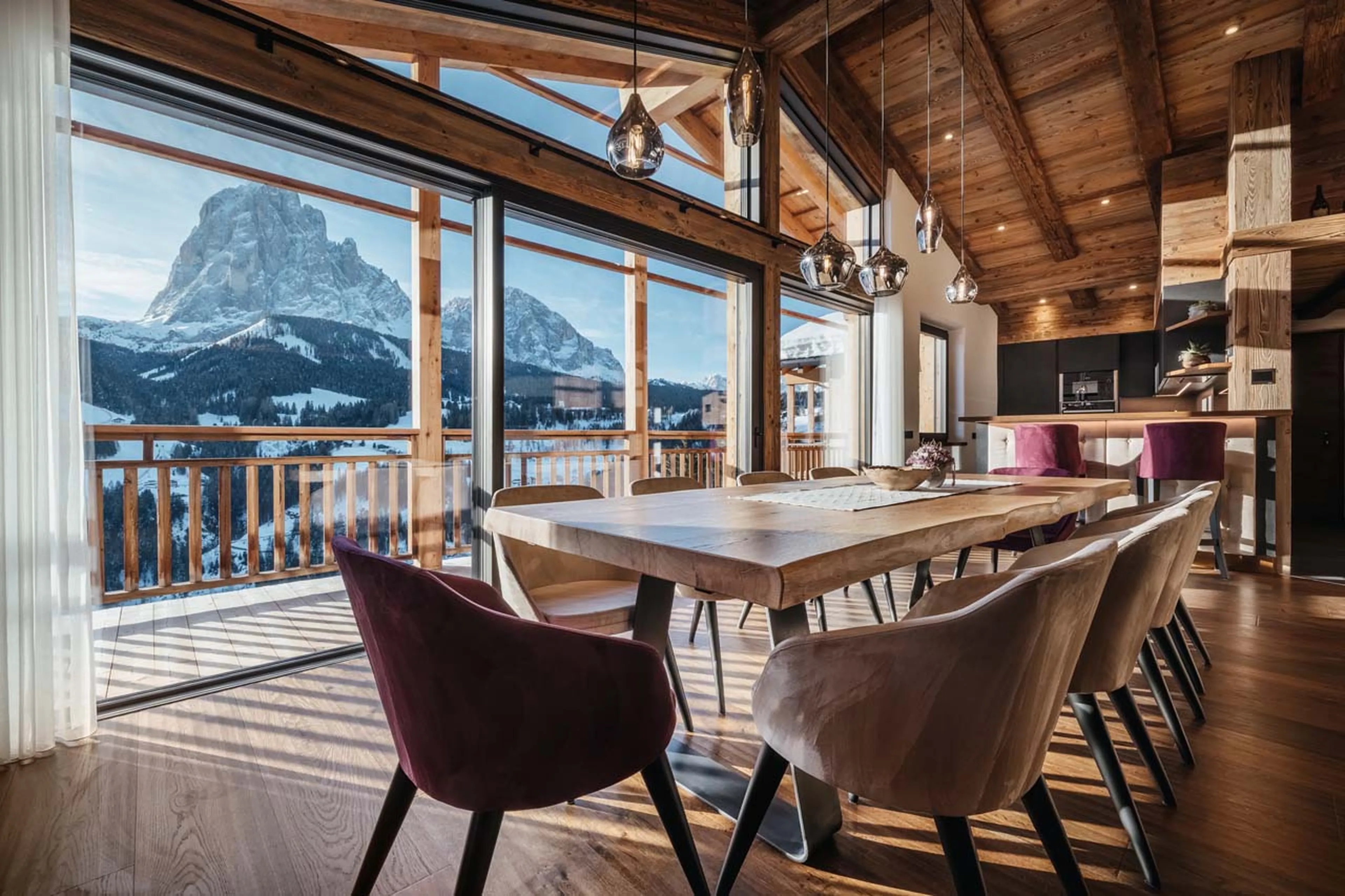 Dining table beneath expansive glass windows in Chalet Robin, Val Gardena